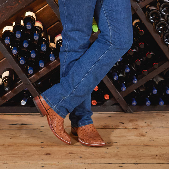 A man wearing Justin Western Boots while standing in front of a wine rack.